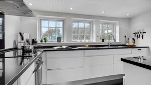 A modern kitchen with a black countertop, white cabinetry, and three windows providing natural light. - 5 bedroom beautiful home in Otterup (Otterup)