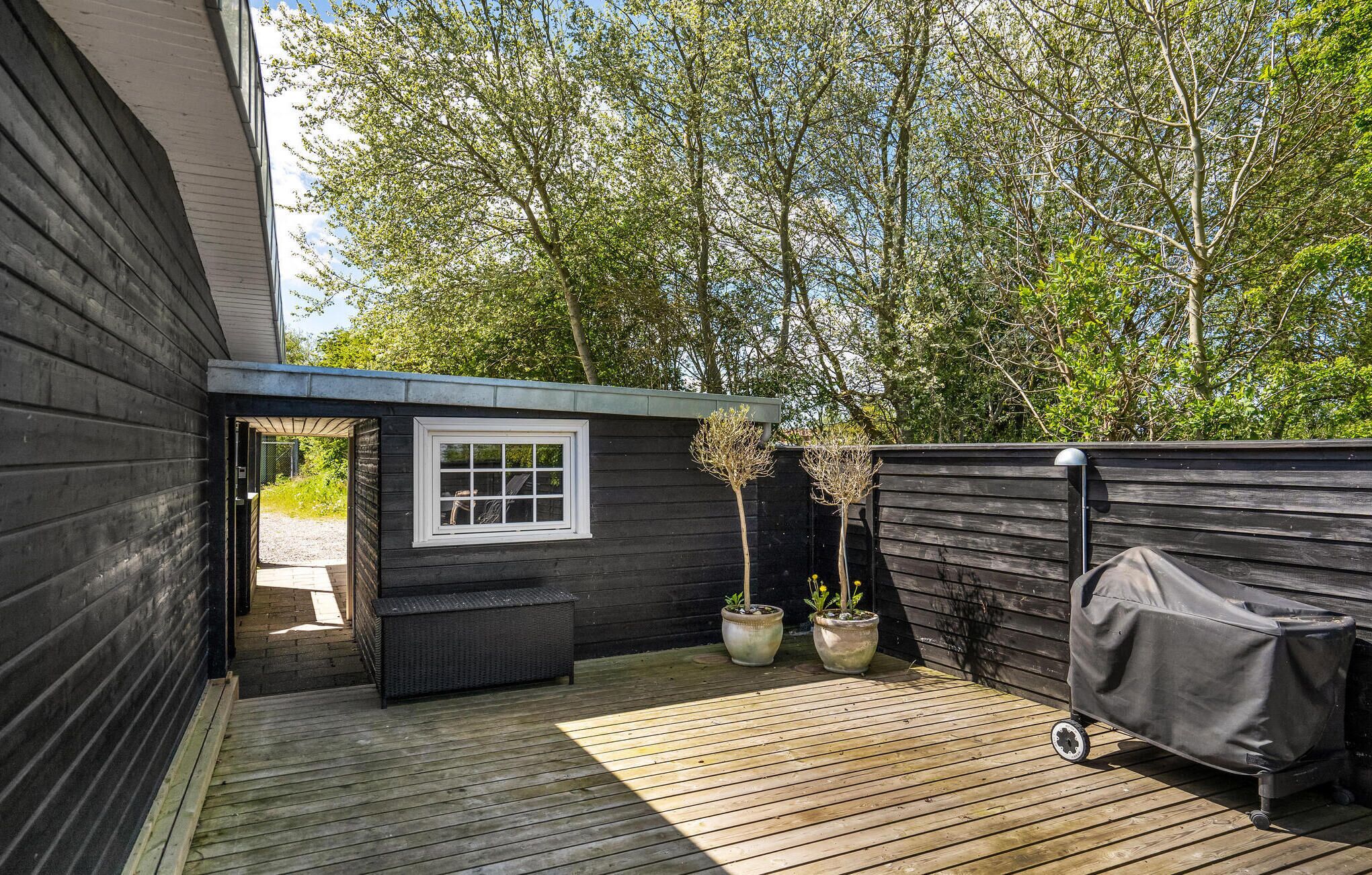 A wooden deck with a covered grill, a small window, and potted plants.