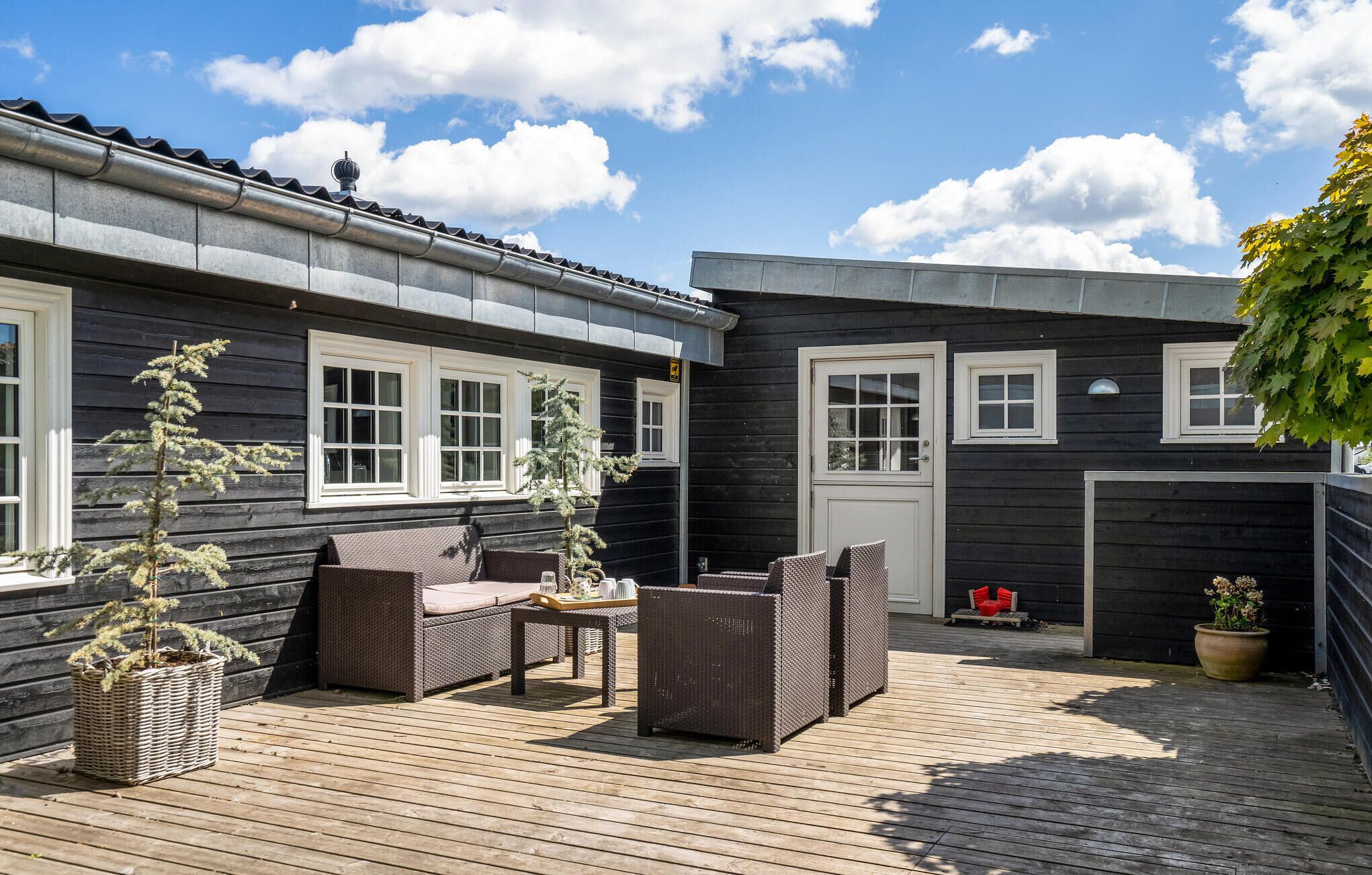 Eine Holzterrasse mit Korbmöbeln, einer Tür und Fenstern.