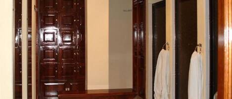 Un pasillo con una puerta de madera, un banco y dos toallas blancas colgadas en ganchos.