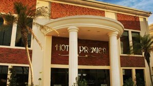 Fachada de hotel com entrada imponente, colunas e uma placa com a inscrição 'HOT PROMIER'.