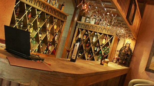 Uma área de bar com prateleiras de madeira repletas de garrafas e copos.