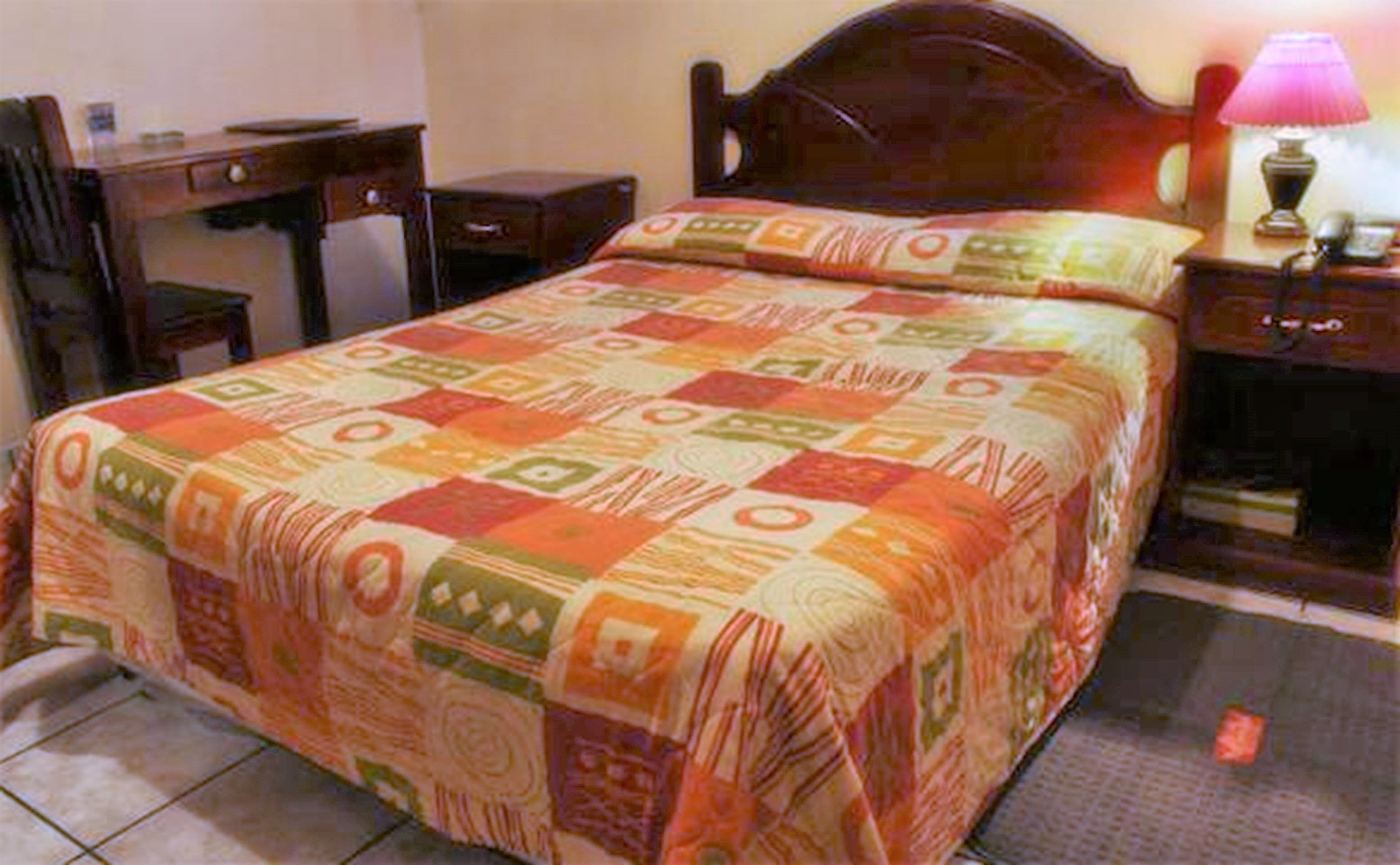 Un dormitorio con cama, mesita de noche, escritorio y lámpara.