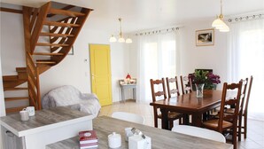 Un coin repas avec une table en bois, des chaises, un vase de fleurs et un escalier.