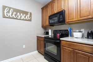 A kitchen with wooden cabinets, a black microwave, a stove, and a kettle. - Amazing  Vista Cay 3 beds/2 bath, Close to Intl Drive , Conv. Center & Sea World. (ORLANDO)