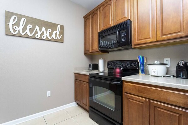 A kitchen with wooden cabinets, a black microwave, a stove, and a kettle.
