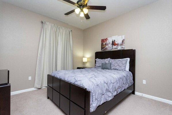 Ein Schlafzimmer mit Bett, Deckenventilator, Nachttisch, Lampe und einem Bild an der Wand.