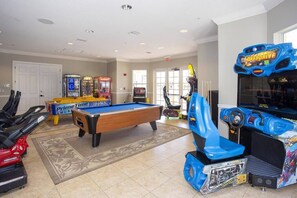 A recreational room with a pool table, arcade games, and a treadmill.
