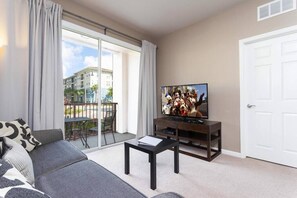 A living room with a sofa, a coffee table, a TV on a wooden stand, and a balcony with a view of buildings.