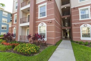 A multi-story residential building with balconies, a central entrance, and a landscaped garden area. - Amazing  Vista Cay 3 beds/2 bath, Close to Intl Drive , Conv. Center & Sea World. (ORLANDO)
