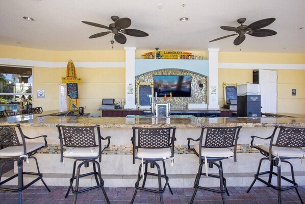 A bar area with a counter, bar stools, ceiling fans, a television, and a sign for 'Land Shark'.