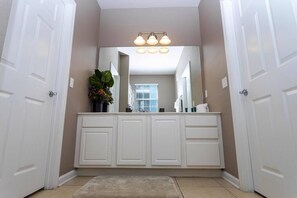 A bathroom with white cabinetry, a large mirror, and a light fixture above the mirror.