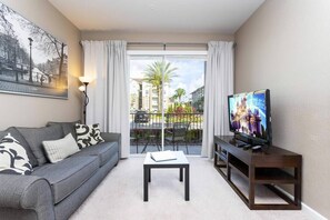 A modern living room with a grey sofa, a coffee table, a TV on a wooden stand, and a large window with curtains. - Amazing  Vista Cay 3 beds/2 bath, Close to Intl Drive , Conv. Center & Sea World. (ORLANDO)