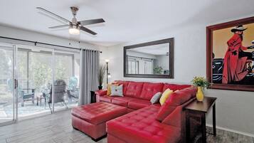 Un salon spacieux avec un canapé en cuir rouge, un ventilateur de plafond, un grand miroir et un tableau accroché au mur.