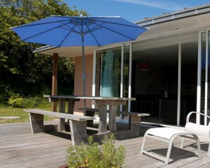 An outdoor patio with a wooden table and benches, a blue umbrella, and a white chair.
