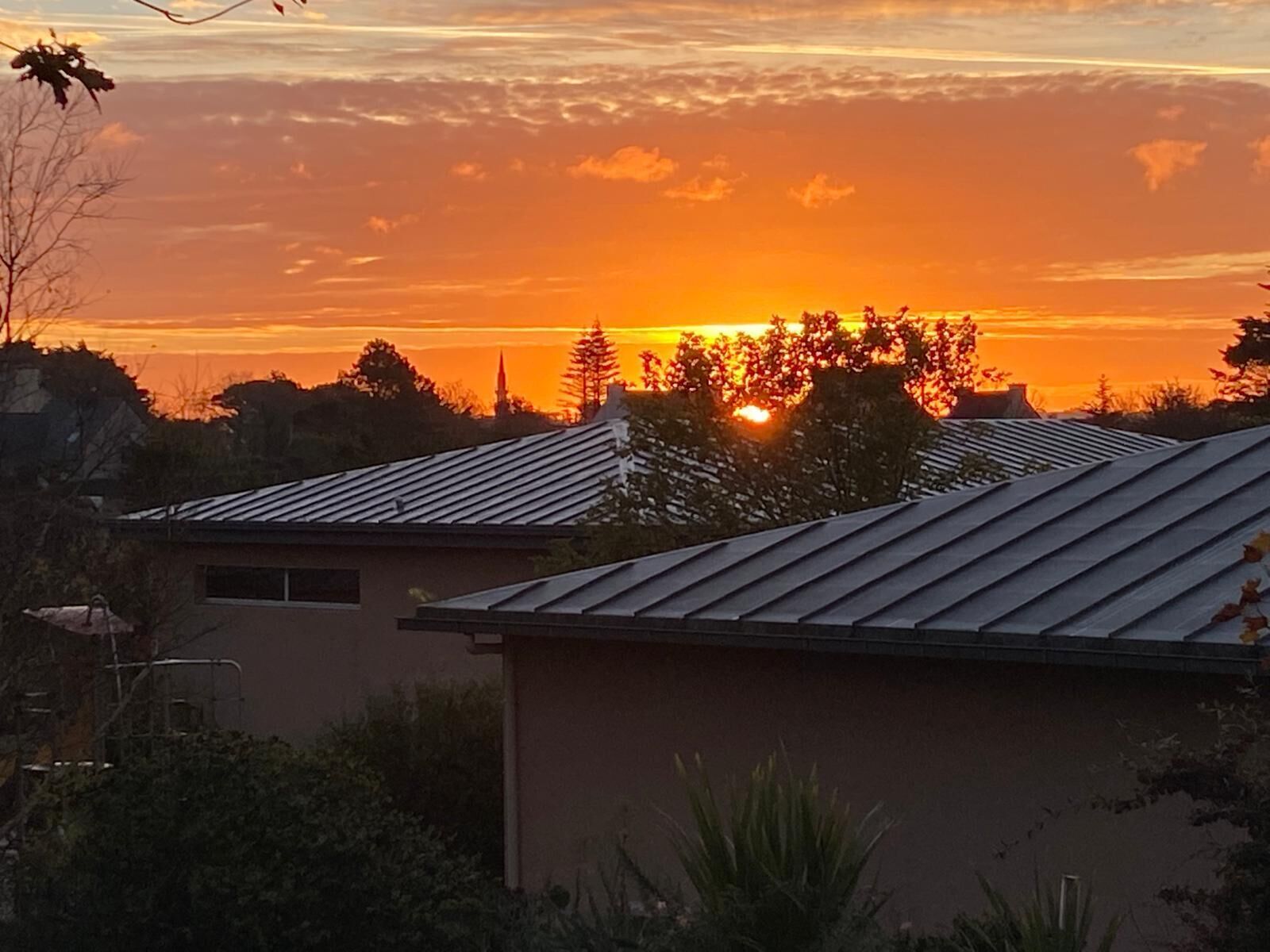 A residential area with houses featuring sloped roofs and a sunset in the background.