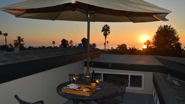 Een terras op het dak met een tafel voor twee, een parasol en uitzicht op de zonsondergang.