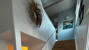Een houten trap met witte leuningen, een aan de muur bevestigd krans, en een ingelijst beeld.