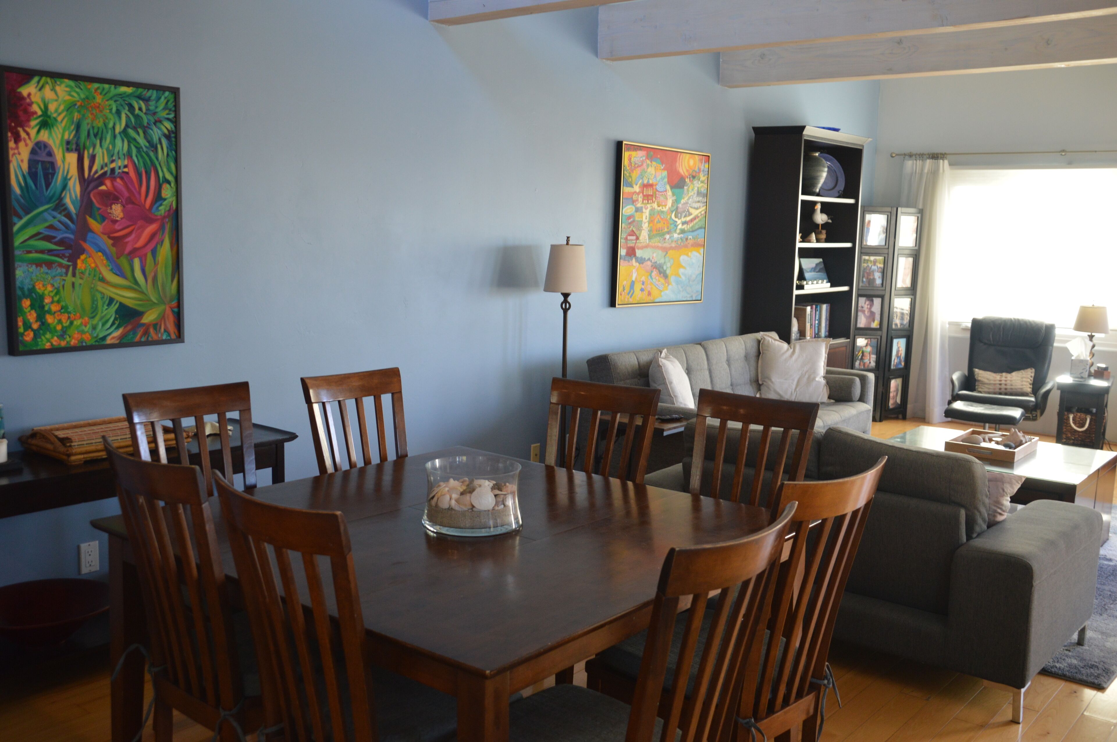 A dining area with a wooden table and chairs, a sofa, and a bookshelf.