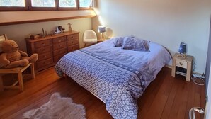 A cozy bedroom with a wooden ceiling, a large bed with patterned bedding, a chair, a dresser, and a window with a view of trees. - Beau Chalet 9 persons, 5 rooms, 120m2 in Allos (Allos)