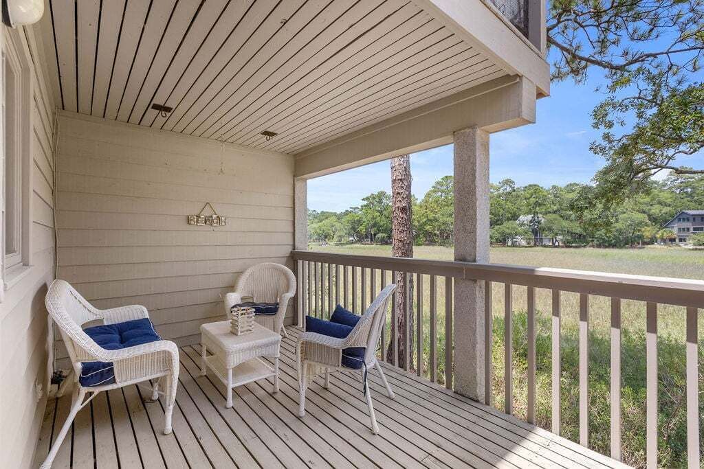 A covered porch with white wicker chairs and a small table, overlooking a grassy area.