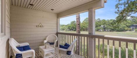 A covered porch with white wicker chairs and a small table, overlooking a grassy area.