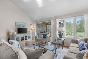 Una sala de estar con sofá, televisor y mesa de centro de vidrio.