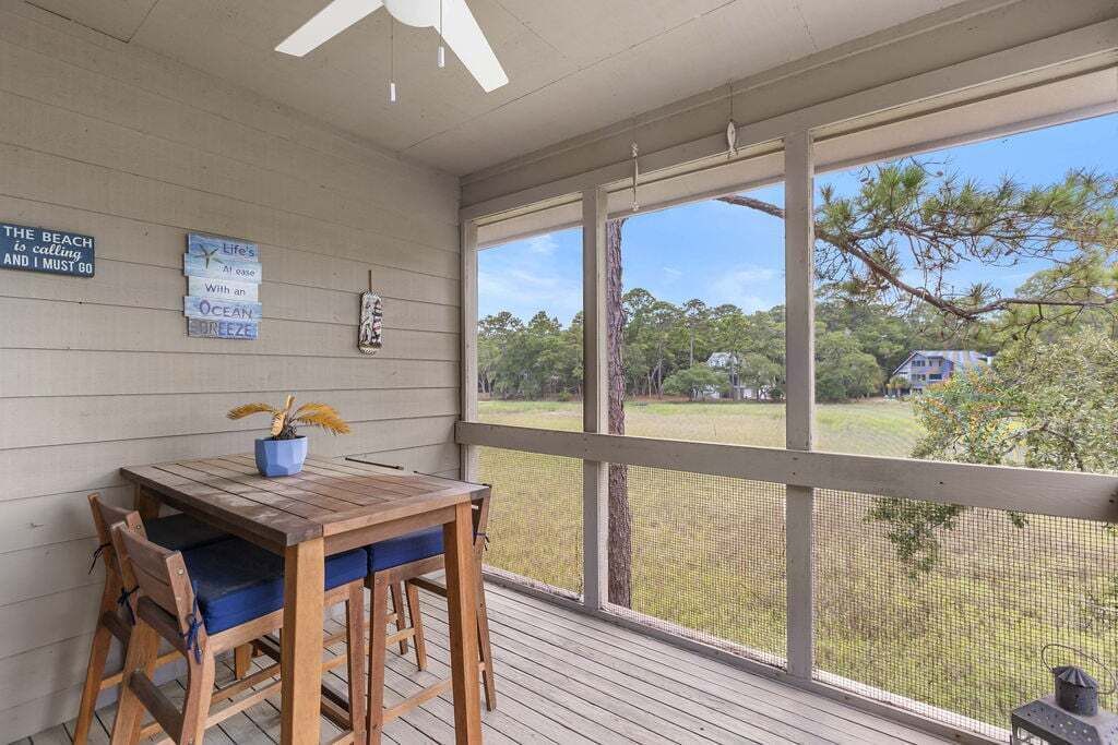 A covered porch with a table and chairs, a view of the outdoors, and wall decorations.