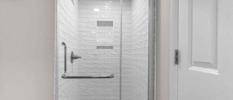 A glass-enclosed shower with white tiled walls, a metal grab bar, and a door with a white frame.