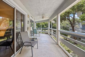 A covered porch with a ceiling fan, sliding glass doors, and a view of trees and a building.