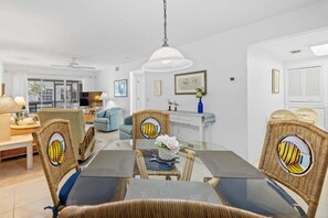 A dining area with wicker chairs, a glass table, and a hanging light fixture.