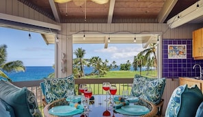 A dining area with a view of the ocean and palm trees, a wooden ceiling, and a purple tiled backsplash.