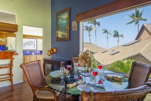Un comedor con sillas de mimbre, una mesa de vidrio y vistas a palmeras.