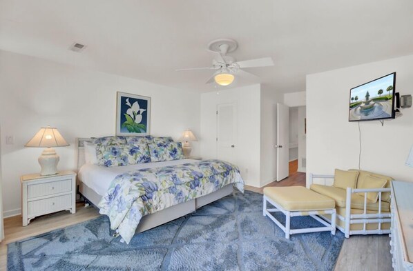A bedroom with a bed, nightstands, a ceiling fan, a TV, and a bench.