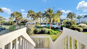 A view from a balcony with a pool, palm trees, and a white building in the background.