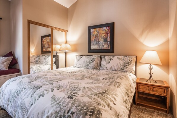 Une chambre à coucher bien rangée, avec un grand lit, une table de chevet avec une lampe, un miroir et un tableau encadré au mur.