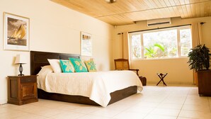 Un dormitorio con cama, mesitas de noche, una ventana con cortinas y una planta.
