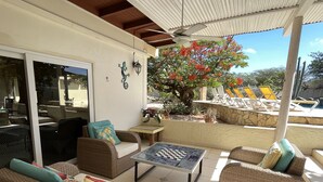 Un espacio al aire libre techado con mobiliario de mimbre, una mesa y vistas a una piscina con sillones de descanso.