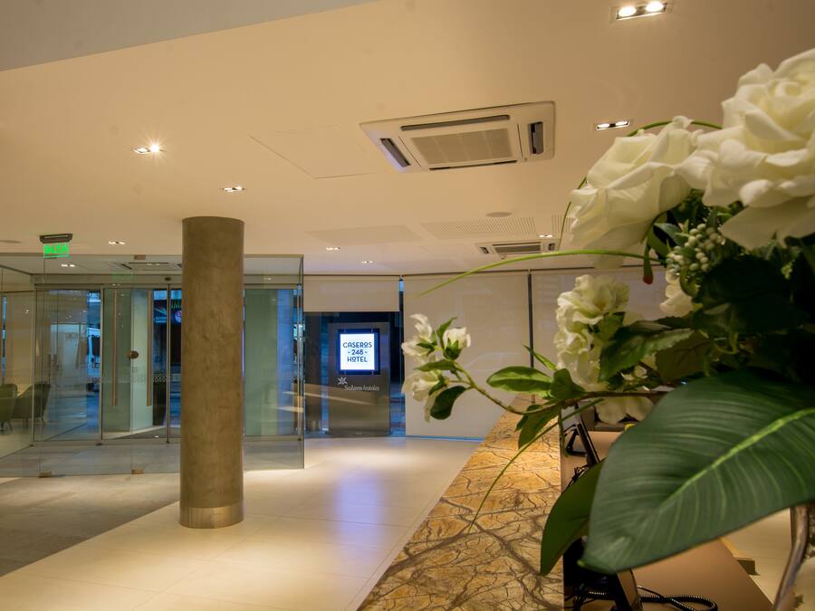 Una hall d'albergo moderna con ingresso in vetro, una reception e un display digitale.