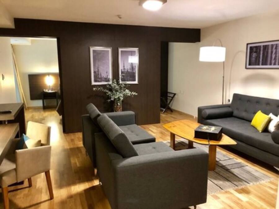 Ett modernt vardagsrum med en soffa, fåtöljer, ett soffbord och ett sidobord. På väggen hänger inramade tavlor och det står en golvlampa i rummet.