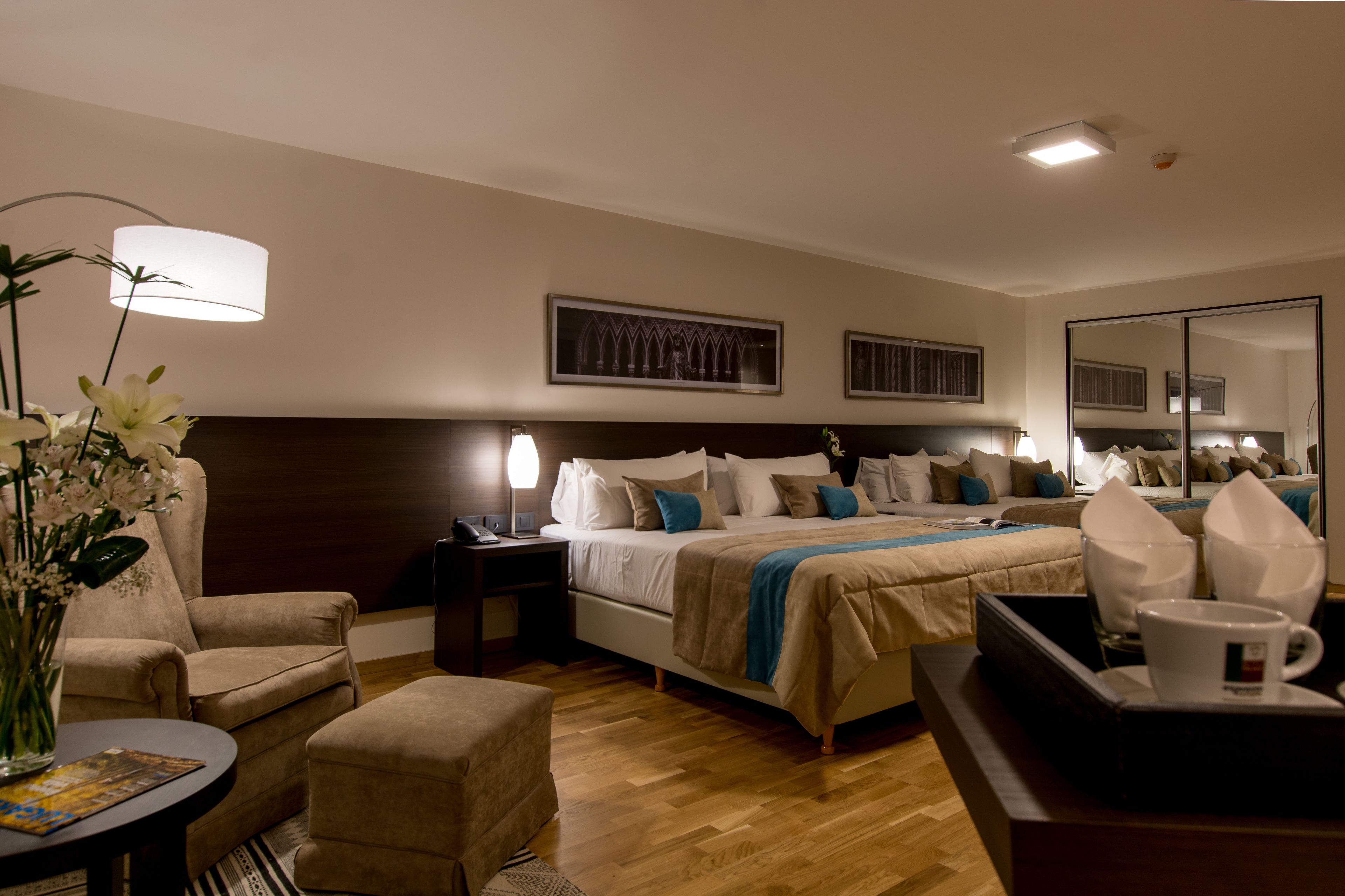 A hotel room with a bed, bedside tables, a chair, a small table with a vase of flowers, and a mirror.
