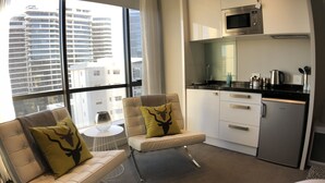 A modern hotel room with a sofa and armchair, a small round table, a kitchenette, and a large window offering a city view. - Sandton Skye Suite 604 (Sandton)