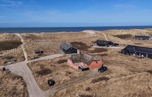 Een landelijk landschap met een opvallend huis met rode dakpannen, verschillende zwarte gebouwen en een helder uitzicht op de zee.