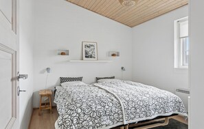 Una camera da letto con un letto, un comodino in legno, una ventola a soffitto, un quadro appeso al muro e una finestra.