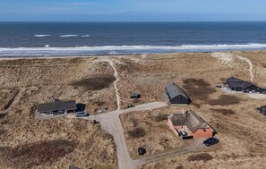 Luchtbeeld van een kustgebied met gebouwen, een weg en windturbines in de verte.