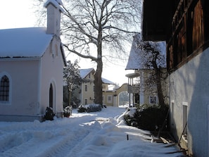 Une rue enneigée bordée d’immeubles, dont une église avec un clocher et une maison jaune dotée d’un balcon.