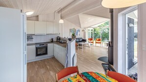 Una cucina moderna con mobili bianchi, forno integrato e zona pranzo con sedie arancioni.