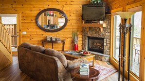 A cozy living room with a stone fireplace, wooden walls, a round mirror, and a comfortable sofa. - ✧ Majestic Cabin - KING bed - NO CLEANING FEE! (Dryfork)