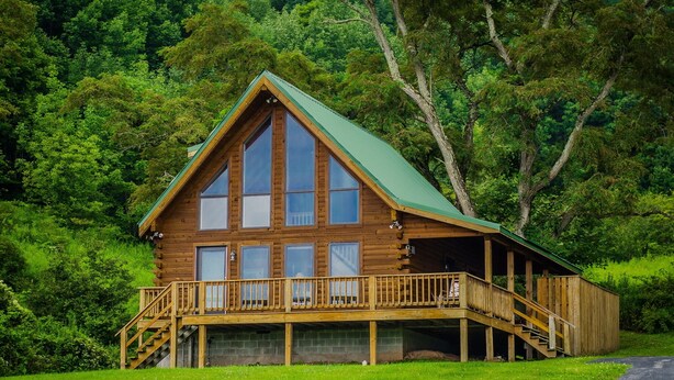 A log cabin with a green roof, large windows, and a wooden deck with stairs leading to a covered porch. - ✧ Majestic Cabin - KING bed - NO CLEANING FEE! (Dryfork)