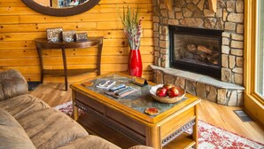 A cozy living room with a stone fireplace, wooden walls, a round mirror, and a comfortable couch. - ✧ Majestic Cabin - KING bed - NO CLEANING FEE! (Dryfork)